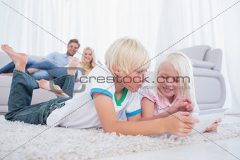 Siblings lying on the carpet using digital tablet