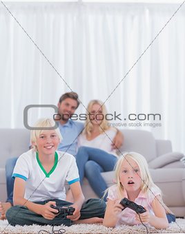 Children on the carpet playing video games while their parents are watching them