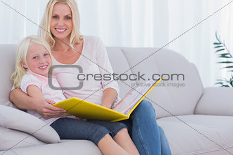 Mother and daughter sitting on couch reading a book