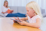 Little girl using tablet while her mother is reading on the couch