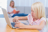 Little girl using laptop while her mother is reading on the couch