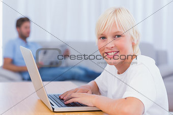 Little boy using laptop while his father is reading on the couch