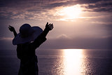 Woman in Hat with Raised Hands Looking at Sunset
