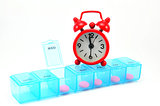 Dialy pill box and red clock on white blackground