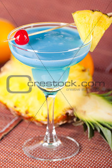 Blue alcohol cocktail with pineapple and cherry