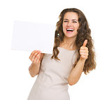 Smiling young woman showing blank paper and thumbs up