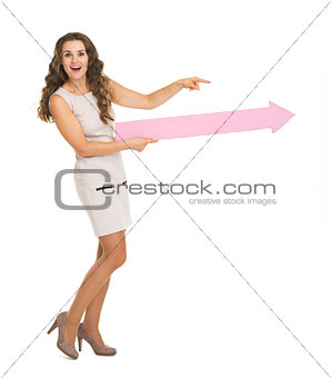 Full length portrait of smiling young woman pointing on copy spa