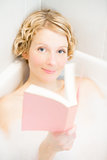 Young woman relaxing and reading a book in the bath