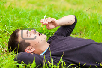 Boy with a cigarette lying in a meadow