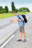Boy hitchhiker on the road waiting for car to stop in summer