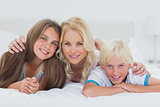Cheerful siblings and mother lying on bed