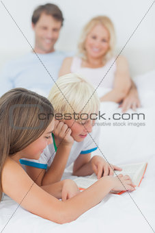Siblings reading a book on the bed