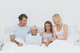 Family sitting in bed and using a laptop