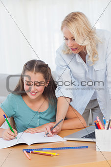 Little girl writing on a book while her mother is helping her