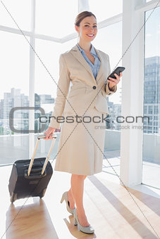Businesswoman walking with suitcase and checking her phone