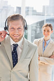 Smiling call centre agent with colleague behind him