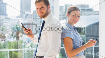 Smiling business team standing back to back and texting
