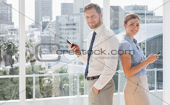 Happy business team standing back to back and texting