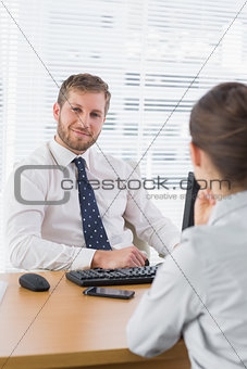 Businessman smiling with a co worker sitting at his desk