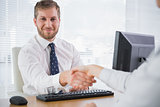 Smiling businessman shaking hands with a co worker and looking at camera