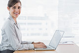 Businesswoman typing on her laptop at desk and smiling at camera