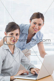 Businesswomen smiling at camera with laptop