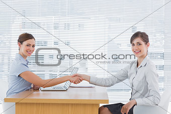 Businesswoman shaking hands with interviewee and both smiling at camera