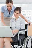 Businesswoman looking at co workers laptop who is sitting in wheelchair
