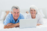 Couple lying and using a laptop in bed
