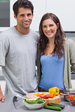 Cheerful couple smiling at camera and preparing vegetables