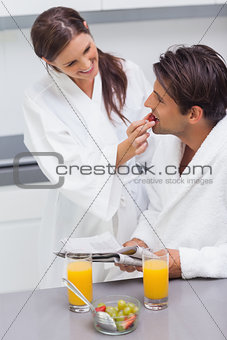 Woman wearing bathrobe feeding her husband strawberry