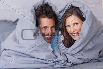 Smiling couple having fun wrapped in their duvet