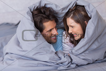 Cheerful couple having fun wrapped in their duvet