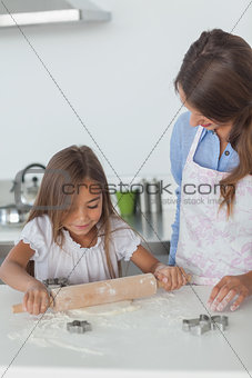 Little girl spreading a dough with a rolling spin