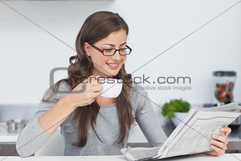 Woman holding a cup of coffee and reading a newspaper