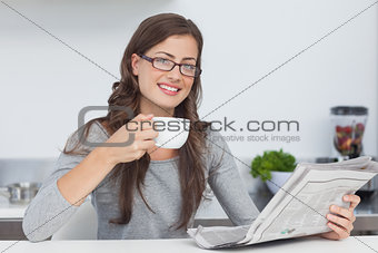 Woman holding a cup of coffee while reading a newspaper