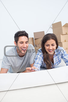 Happy couple lying on the floor and holding a house plan