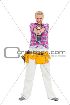 Blonde standing while pointing a drill at camera