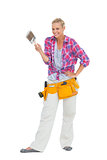 Smiling woman holding paint brush wearing a tool belt