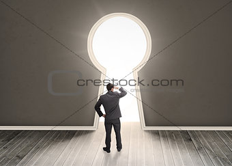 Businessman looking through a keyhole shape door