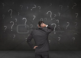 Rear view of a doubtful businessman looking at various question marks