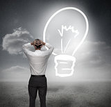 Businessman looking at light bulb with hands on head