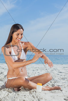 Smiling woman sitting on beach applying sunscreen