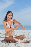Happy woman sitting on beach applying sunscreen