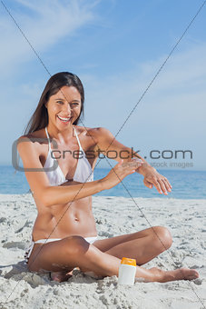 Happy woman sitting on beach applying sunscreen