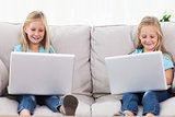 Young twins using laptops sitting on a couch