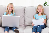 Twins using a laptop and a tablet sitting on a couch
