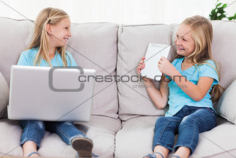 Young twins using a laptop and a tablet sitting on a couch