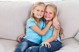 Cute twins embracing each other sitting on a couch