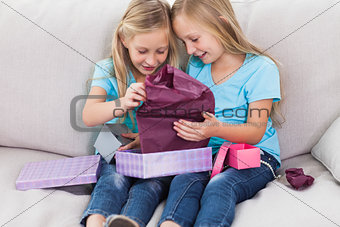 Young twins unwrapping birthday gift sitting on a couch
